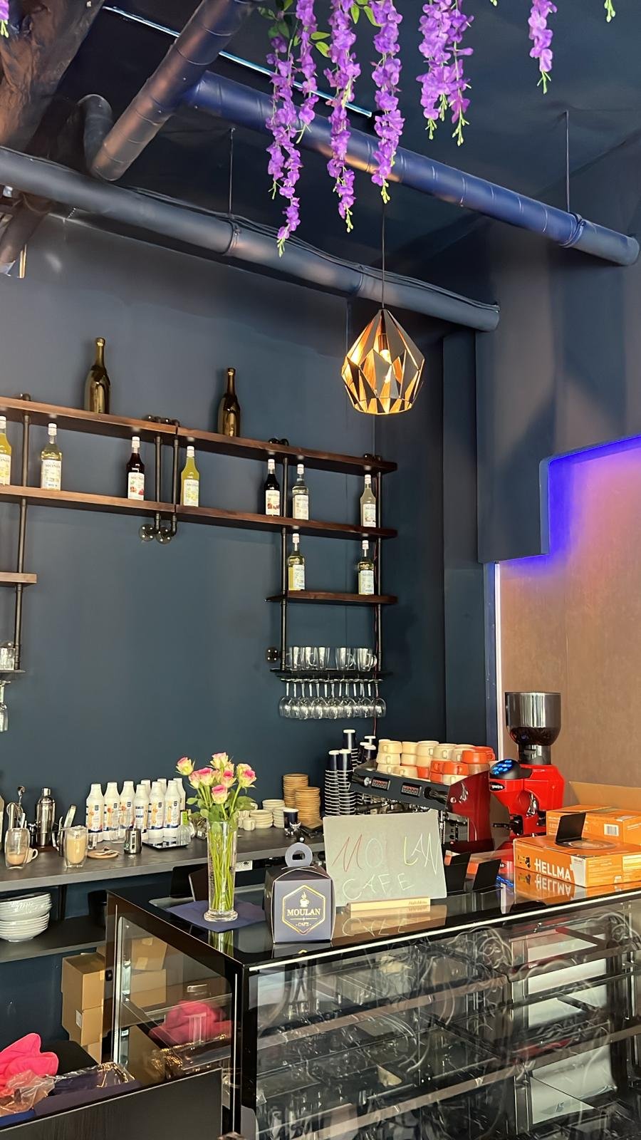 Gemütliches Interieur des Moulan Café mit Holzregalen, Gläsern und warmen Hängeleuchten